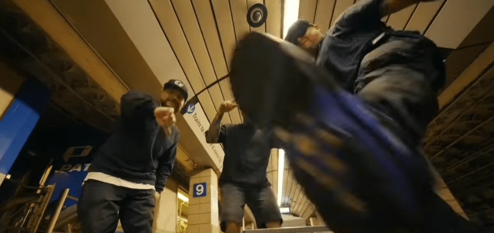 Three people performing a dance pose in a subway station, with one person prominently kicking their foot forward.