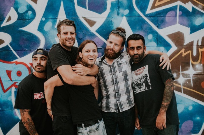 A group of five friends posing together in front of a colorful graffiti wall, smiling and embracing each other.