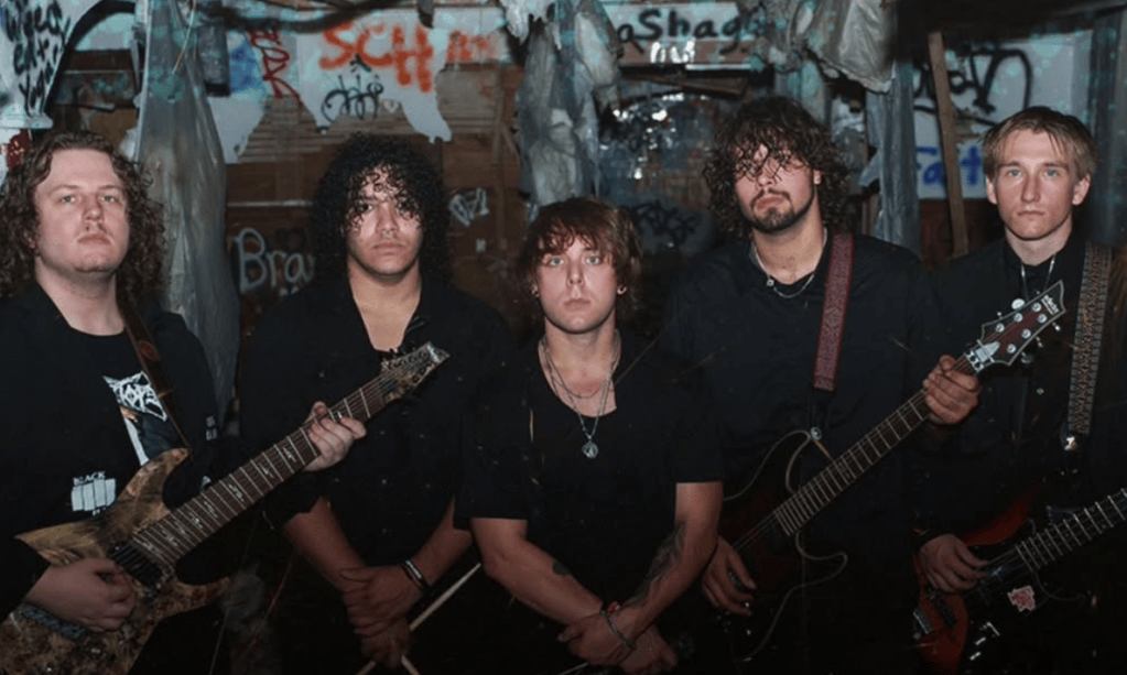 A rock band posing together in a dimly lit, graffiti-covered space. The members are dressed in dark clothing, with several holding electric guitars.