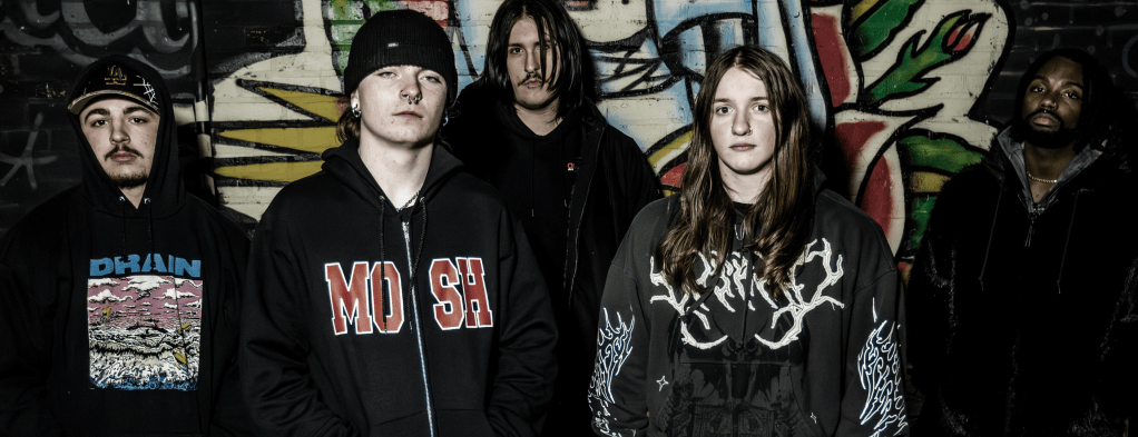 Five musicians posing in front of a colorful graffiti wall, wearing hoodies and streetwear, with various expressions.
