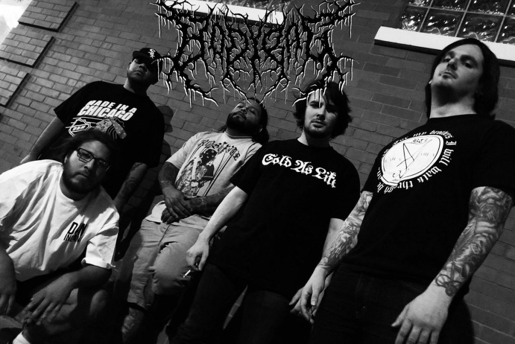 A black and white image of a five-member metal band posing in front of a brick wall, dressed in band t-shirts.